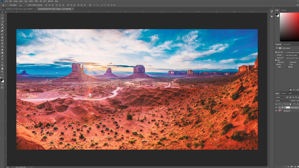 En computerskærm viser Adobe Photoshop i redigeringstilstand med et levende landskabsbillede af Monument Valley og forskellige værktøjspaneler åbne, perfekt til dem, der ønsker at opret trykfiler med dramatiske røde klippeformationer og en slående himmel.