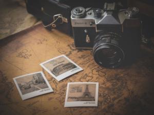 Et vintage Zenit-E-kamera hviler på et gammelt kort ved siden af tre sepia-tonede øjeblikkelige billeder, deres kanter blødgjort som af en vignet i Photoshop, med vartegn som Eiffeltårnet i Paris. En kamerataskerem er synlig i baggrunden.