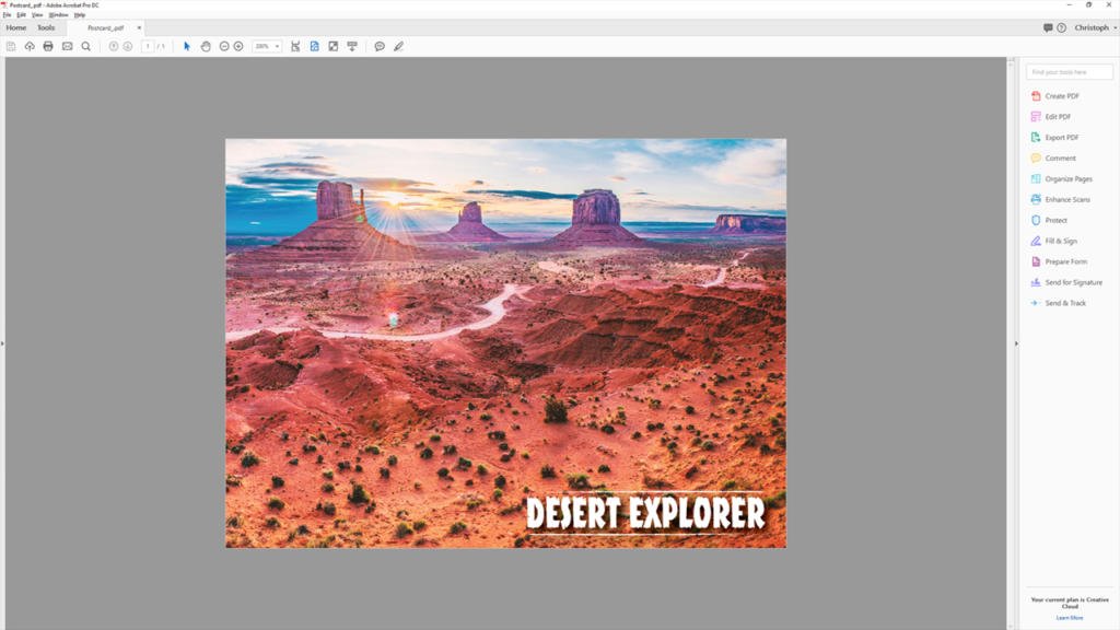 Et PDF-dokument åbent på en computerskærm viser et levende ørkenlandskab med mesas, rødt sand og en snoet vej ved solnedgang. Teksten DESERT EXPLORER og opret trykfiler vises med fede hvide bogstaver i nederste højre hjørne.