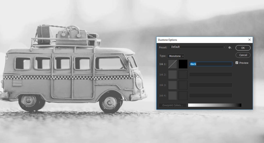Et sort-hvidt foto af en legetøjsvogn med bagage på toppen. I forgrunden er en grafisk redigeringssoftware-dialogboks for duotone-indstillinger åben, som viser indstillinger for en sepia monoton effekt.